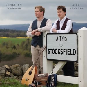 Alex and Jonathan lean against a sign post reading "A Trip to Stocksfield"