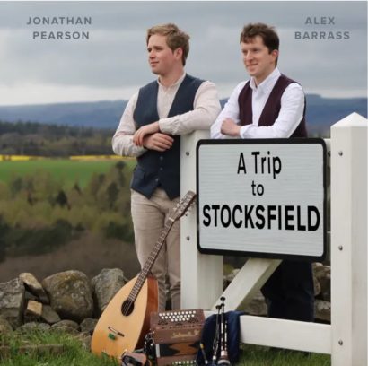 Alex and Jonathan lean against a sign post reading "A Trip to Stocksfield"
